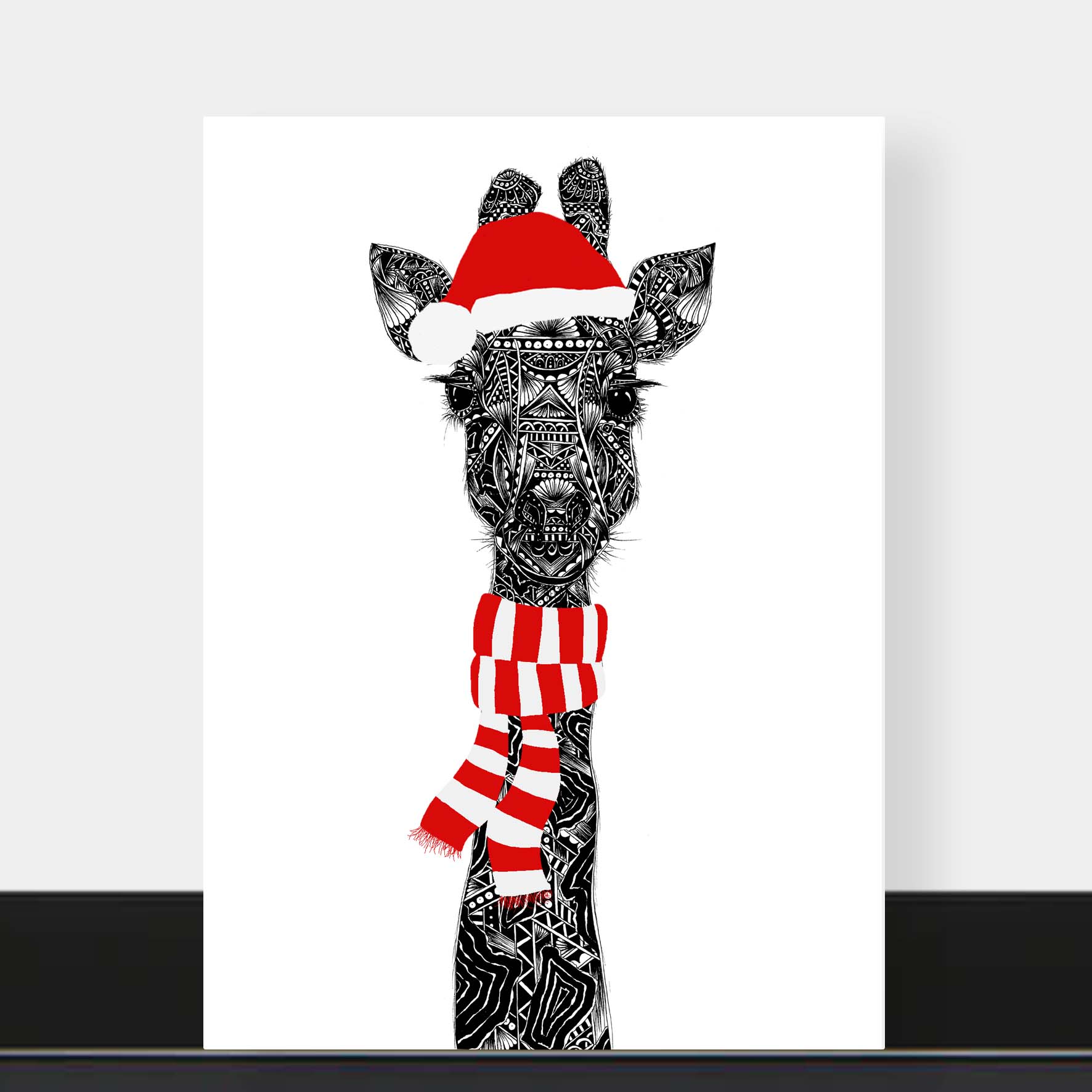 Christmas card of a giraffe wearing a Santa hat and scarf on a white background