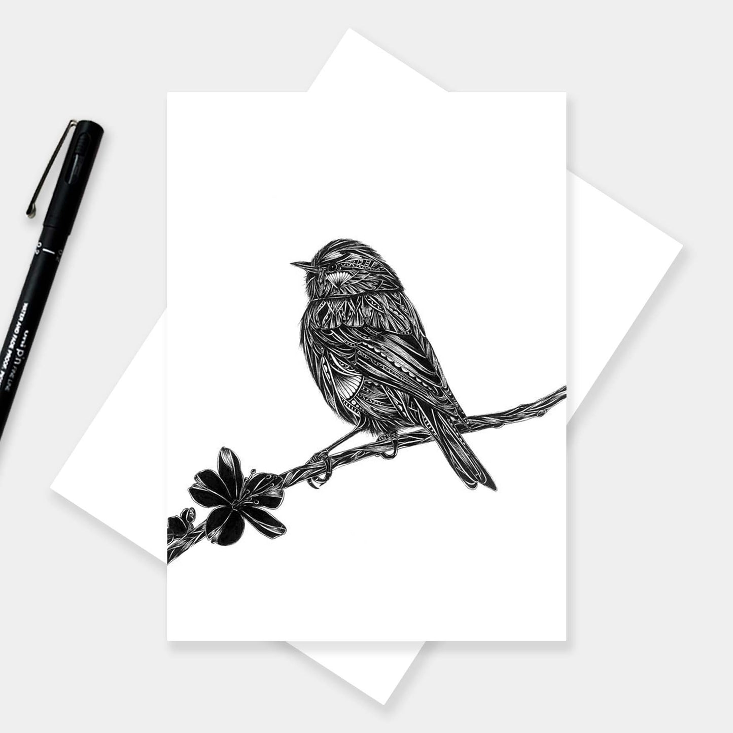 Intricate black and white blue tit greetings card on white envelope with pen next to it