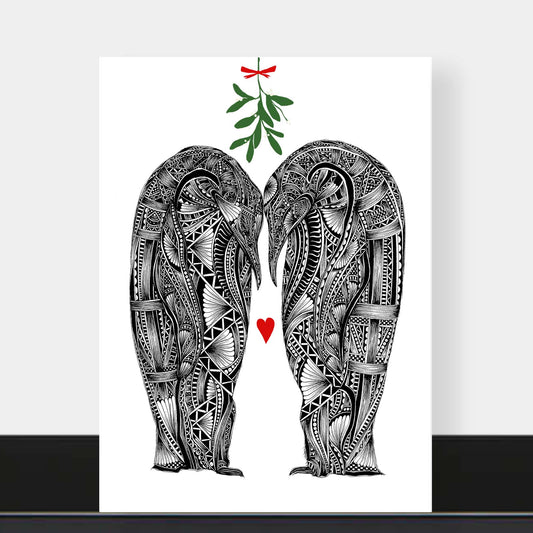 Christmas love greetings card featuring two black and white penguins with their heads together with green mistletoe above with red bow and love heart in-between them and white background. The card is on a black shelf with a grey background