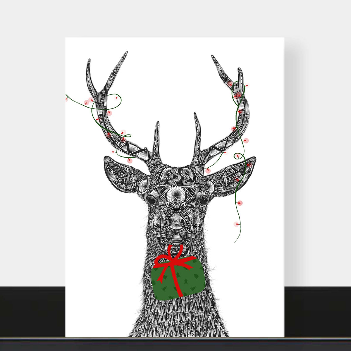 Black and white illustration of stag on greetings card with green and red Christmas present and lights on a white background