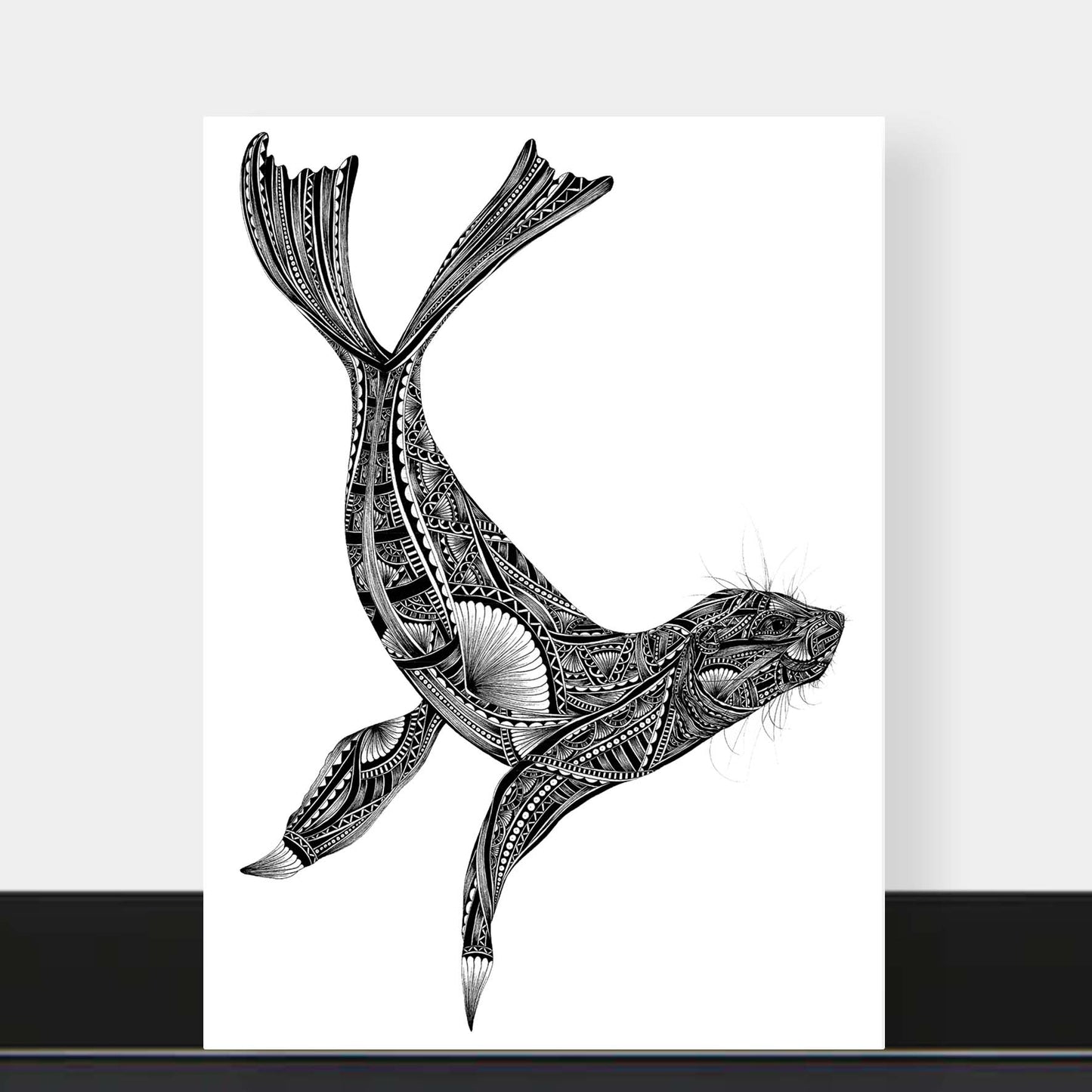 A vertical art print featuring a black and white hand-drawn seal with intricate tribal patterns, displayed against a light gray wall with a black shelf below.