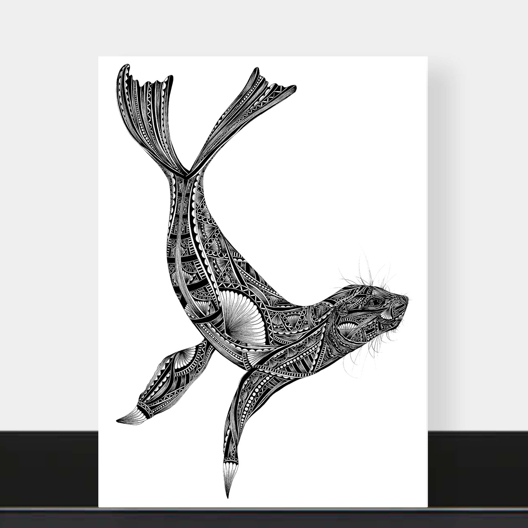 A vertical art print featuring a black and white hand-drawn seal with intricate tribal patterns, displayed against a light gray wall with a black shelf below.